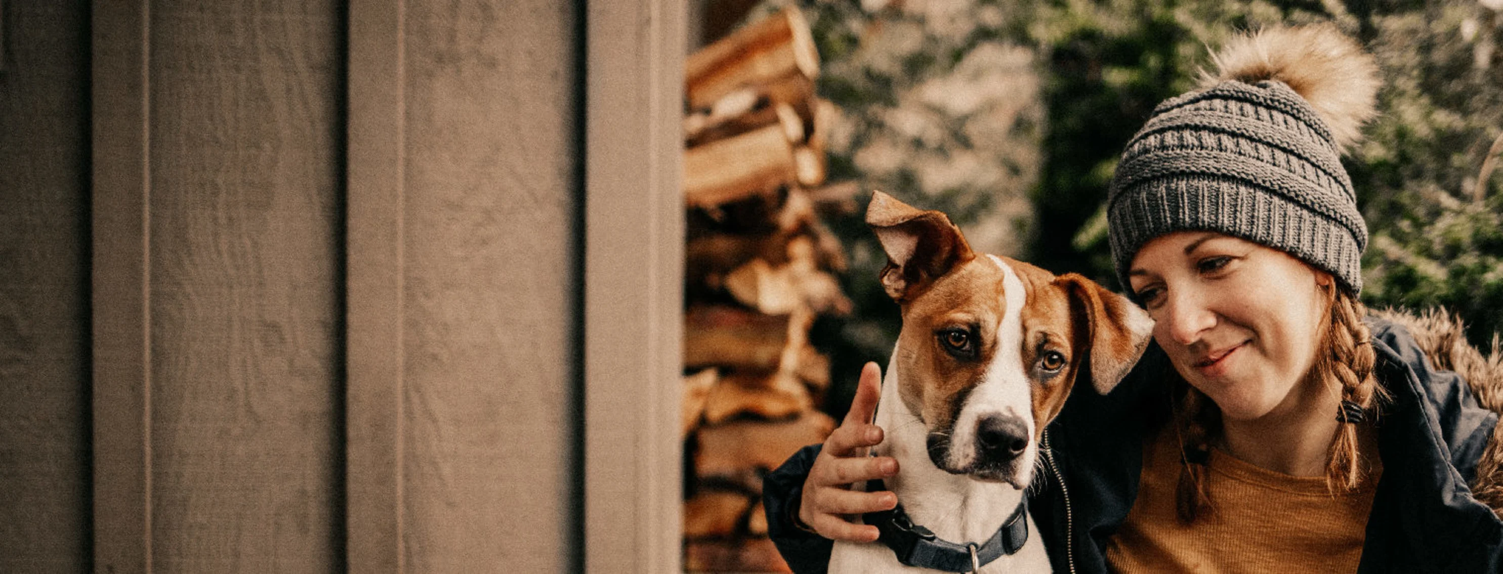 A dog snuggling with its owner outdoors next to a stack of firewood